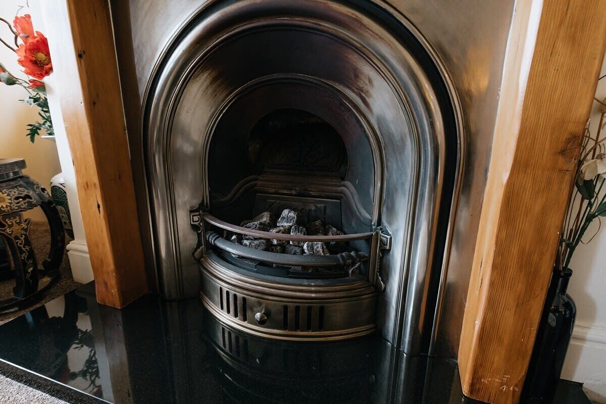 A fireplace with a metal arch and a wooden frame, set in a room with a polished floor and a vase with flowers.