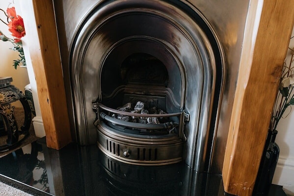 Una chimenea con un arco de metal y un marco de madera, ubicada en una habitación con piso pulido y un florero con flores.