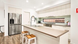 A modern kitchen with stainless steel appliances, a central island with stools, and a backsplash with a wood-like pattern. - Boobook Retreat in Cowes (Cowes)