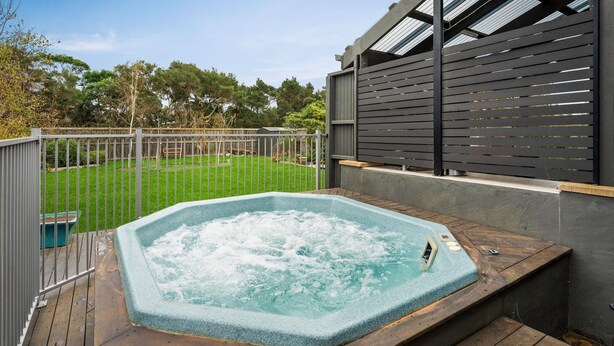 A hot tub on a wooden deck with a metal fence and a grassy yard in the background. - Boobook Retreat in Cowes (Cowes)