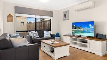 A modern living room with a sofa, coffee table, and TV. There is a window with a view of the outside, a wicker basket, and a framed picture on the wall.