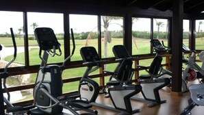 Et fitnessrum med motionscykler og løbebånd, store vinduer med udsigt over en golfbane.