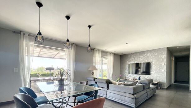 Una sala de estar moderna con una mesa de comedor de cristal, sofás grises y un televisor de pantalla plana montado en la pared.