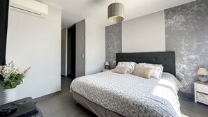 Un dormitorio moderno con una cama grande, una mesita de noche, una lámpara y aire acondicionado instalado en la pared.