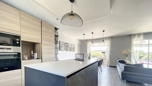 Una cocina moderna con una isla central, electrodomésticos integrados e iluminación colgante.