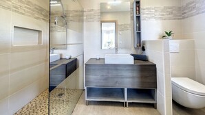 Un baño moderno con cabina de ducha de vidrio, un espejo grande, dos lavamanos y un inodoro.