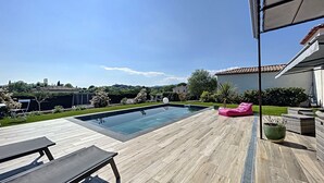 Un patio trasero con piscina, terraza de madera y mobiliario exterior.