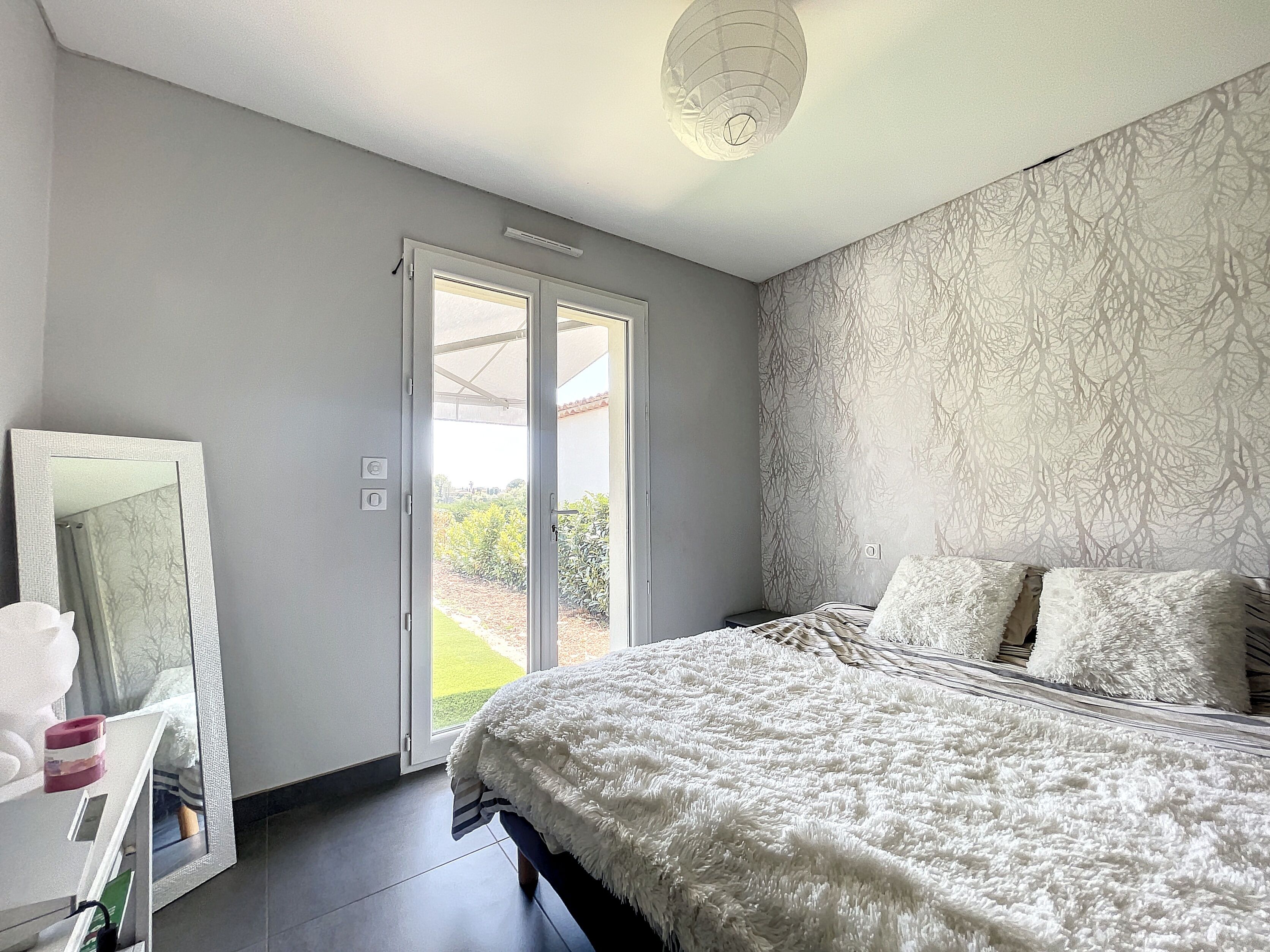 A bedroom with a bed, a large mirror, and a sliding glass door leading to a garden.