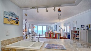 Una cocina amplia con una isla grande, un comedor con sillas coloridas y vistas al mar a través de ventanas enormes.