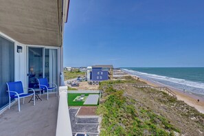 Un balcon avec des chaises bleues, une vue sur la plage et un immeuble à la façade bleue.