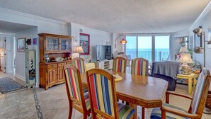 Un amplio salón con una mesa de comedor, sillas a rayas, un aparador de madera y un gran ventanal con vistas al mar.