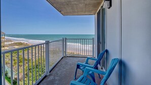 Un balcón con vista a la playa, techo de hormigón y barandilla blanca.