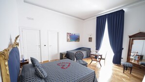 Et hotelværelse med en stor seng, en mindre seng, et skrivebord med stol, et spejl og et billede på væggen.