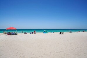 A beach with a red tent, a blue tent, and several beach chairs. - Southwind #J2| Updated Ground Floor Beach Condo (Panama City Beach)