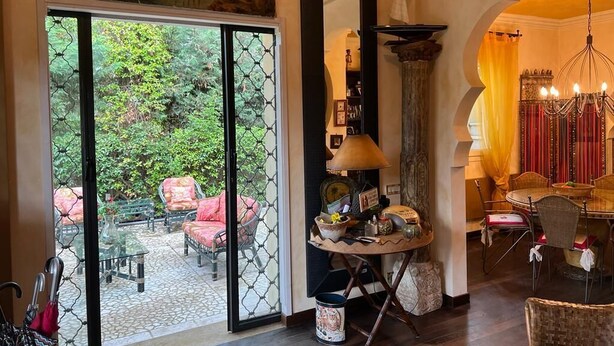 A room with a large glass door leading to an outdoor area with chairs and a table. There is a round table with various items on it, a tall column, and a chandelier. - Villa MIMA with garden on two floors, 100 m from the sea. (Milano Marittima)