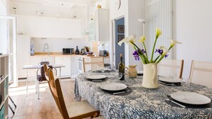 A dining area with a table set for two, a vase with flowers, and a kitchen in the background. - 450 m from the beach – House for 6 – Garden & BBQ (Treffiagat)