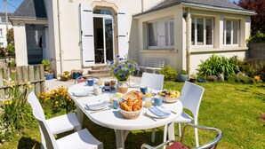 A dining table set outdoors with food and drinks, surrounded by chairs, in front of a house with a garden. - 450 m from the beach – House for 6 – Garden & BBQ (Treffiagat)