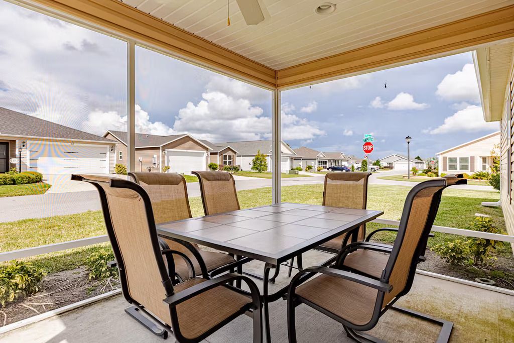 A covered patio area with a table and chairs, overlooking a residential street.