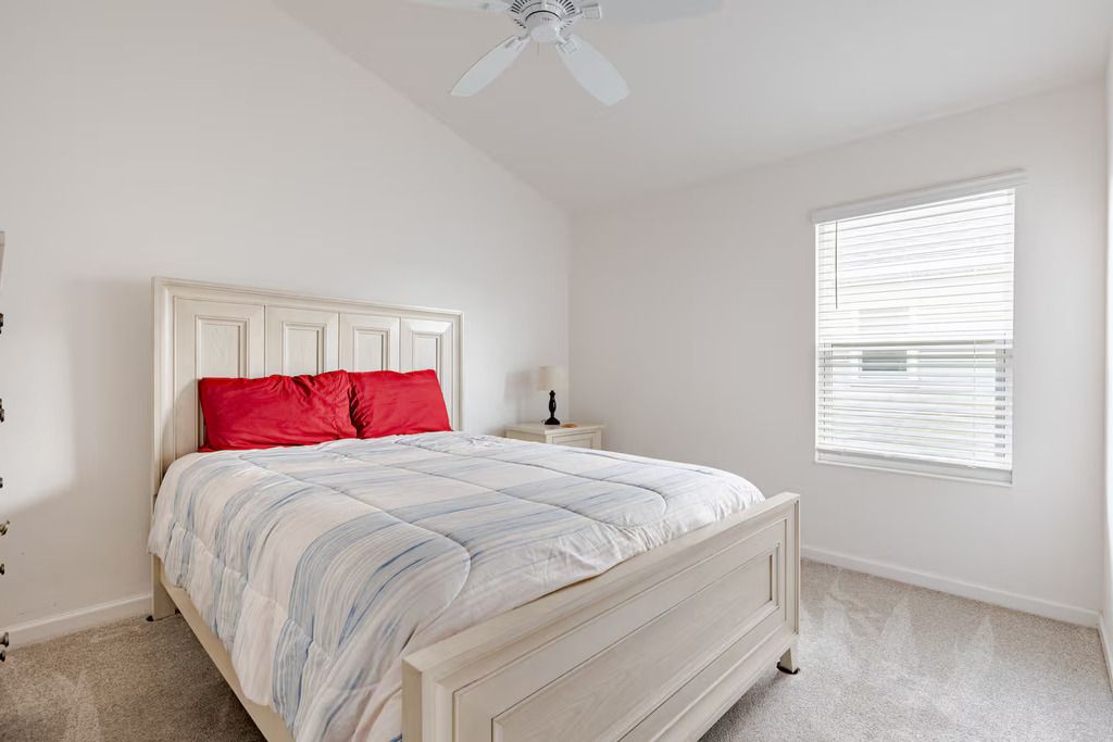 Quarto com cama, mesa de cabeceira, janela com persianas e ventilador de teto.