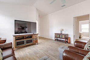 A living room with a flat-screen TV, wooden entertainment unit, leather sofas, and a small side table.