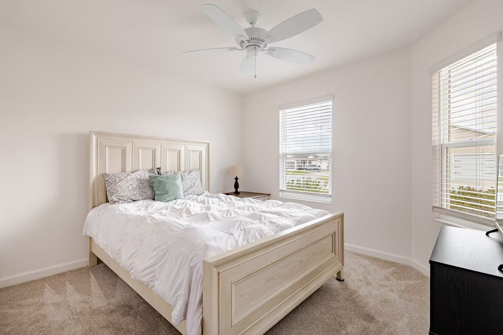 Ein Schlafzimmer mit Bett, Deckenventilator, Fenster mit Jalousien und einem Schminktisch.