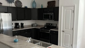 Une cuisine moderne avec des meubles de couleur sombre, un réfrigérateur en acier inoxydable, un four à micro-ondes et une cuisinière.