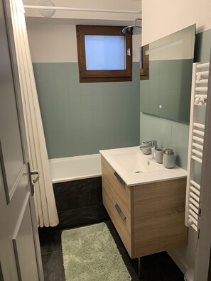 Un baño con tocador de madera, bañera, ventana y perchero para toallas.