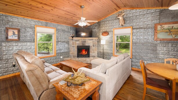 A cozy living room with a stone fireplace, leather sofa, and a dining table. - Elevated Farm Cabin | River Views & Access, Hot Tub & Thoughtful Finishes (Steelville)
