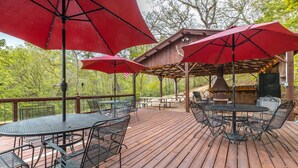 A wooden deck with outdoor seating, including tables and chairs, and red umbrellas providing shade. - Elevated Farm Cabin | River Views & Access, Hot Tub & Thoughtful Finishes (Steelville)