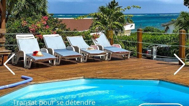 Área à beira da piscina com espreguiçadeiras e vista para o mar.