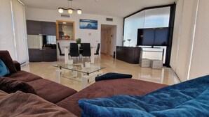 A modern living room with a brown sofa, a glass coffee table, and a TV. - Solbelli Oceanfront Penthouse | Jacuzzi (Mijas Costa (Riviera del Sol))