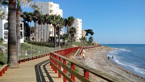 A wooden boardwalk with red railings leading to a beach. - Solbelli Oceanfront Penthouse | Jacuzzi (Mijas Costa (Riviera del Sol))