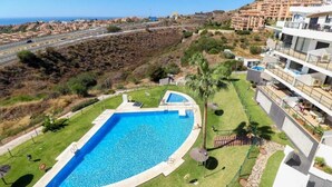 A swimming pool surrounded by a well-maintained lawn, a stone pathway, and a view of a coastal road. - Solbelli Oceanfront Penthouse | Jacuzzi (Mijas Costa (Riviera del Sol))
