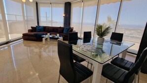 A modern living room with a glass table, black chairs, a brown sofa with blue cushions, and a potted plant. - Solbelli Oceanfront Penthouse | Jacuzzi (Mijas Costa (Riviera del Sol))