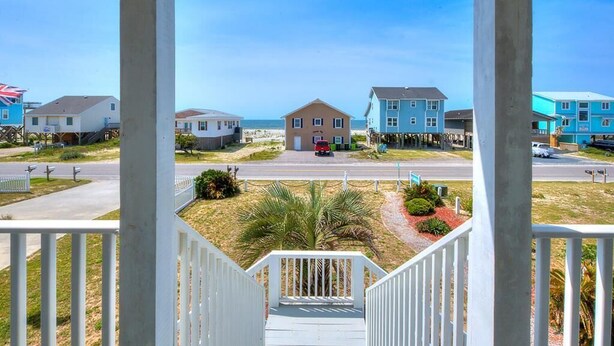 A coastal residential area with houses on stilts, a clear sky, and a road in the foreground. - 2nd Row Oceanview Home with Private Pool, Zzzs by the Beach (Oak Island)