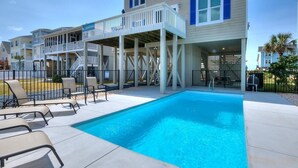 A swimming pool with lounge chairs, a covered deck, and a building with a balcony. - 2nd Row Oceanview Home with Private Pool, Zzzs by the Beach (Oak Island)