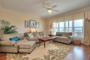 A living room with beige sofas, a wooden coffee table, and a large window with a view.