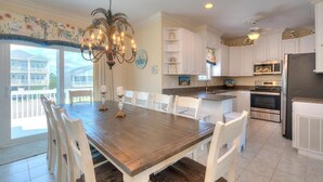 A spacious kitchen with white cabinetry, a dining table with chairs, a chandelier, and a view of a house through the window. - 2nd Row Oceanview Home with Private Pool, Zzzs by the Beach (Oak Island)