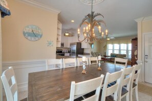 A dining area with a wooden table and white chairs, a chandelier, and a clock on the wall.