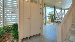 A hallway with a wooden staircase, a beige door with a green sign, and a view of the outside. - 2nd Row Oceanview Home with Private Pool, Zzzs by the Beach (Oak Island)