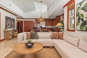 A modern living room with a sectional sofa, a round wooden coffee table, and a kitchen in the background.