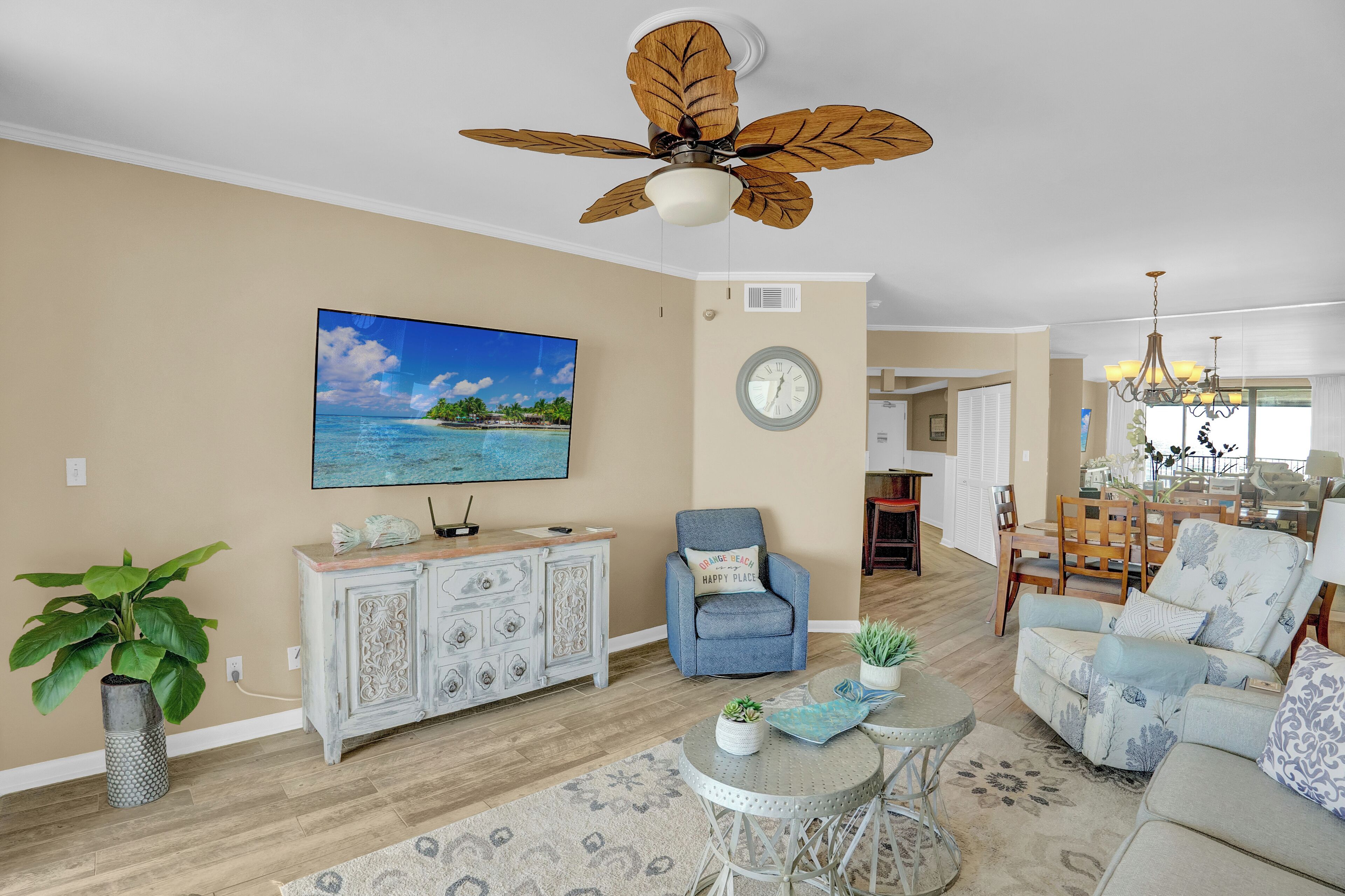 A living room with a ceiling fan, a television, a clock, and a dining area with chairs and a table.