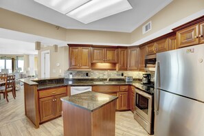 A modern kitchen with wooden cabinets, a stainless steel refrigerator, and a large island with a granite countertop.