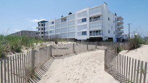 A multi-story hotel with a sandy beach path leading to the entrance, surrounded by a wooden fence. - DAILY ACTIVITIES & LINENS INCLUDED! 3BR, 2BA Condo with a Large Balcony. Great mid-town location! (Ocean City)