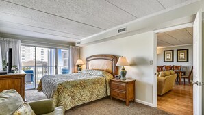 A hotel room with a large bed, two bedside tables, a chair, a small table, and a view of the city through the window.