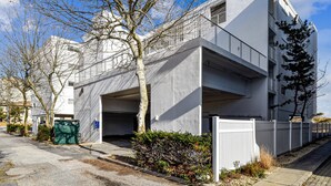 A modern two-story building with a flat roof, a garage, and a white fence.
