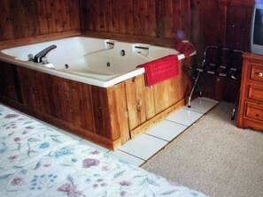 Une baignoire en bois avec une serviette rouge, un meuble en bois et une couvre-lit à motifs floraux.