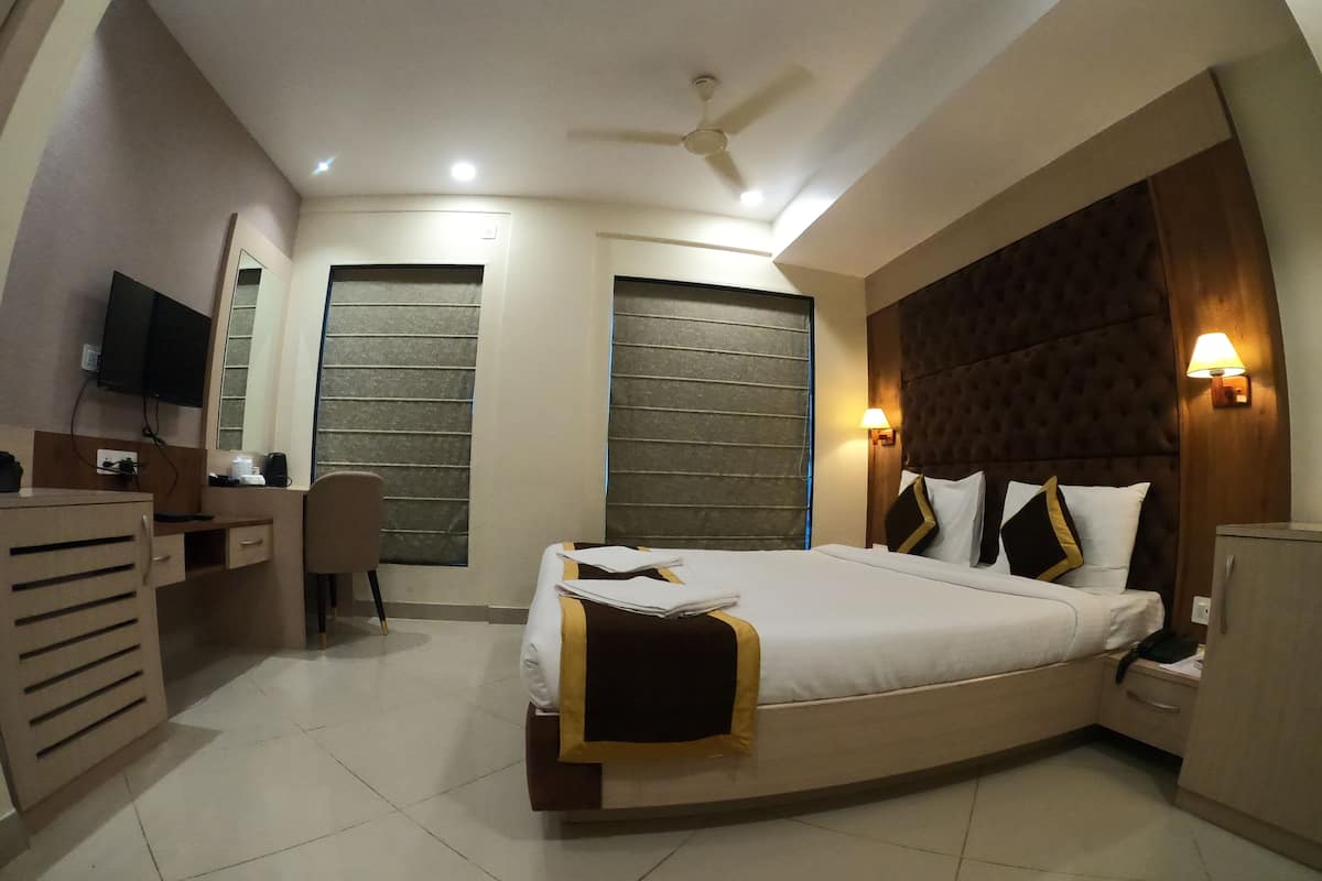 A hotel room with a bed, desk, chair, and a TV mounted on the wall.