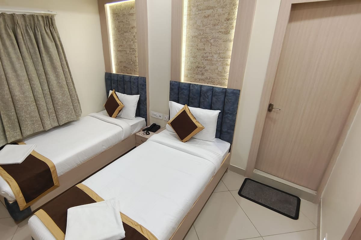 A hotel room with two single beds, a wardrobe, a window with a brick pattern, and a curtain.