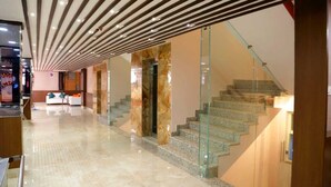 A modern hotel lobby with a marble floor, a glass staircase, and a reception area with a white sofa. - The Panash Hotel & Banquets (Kolkata)